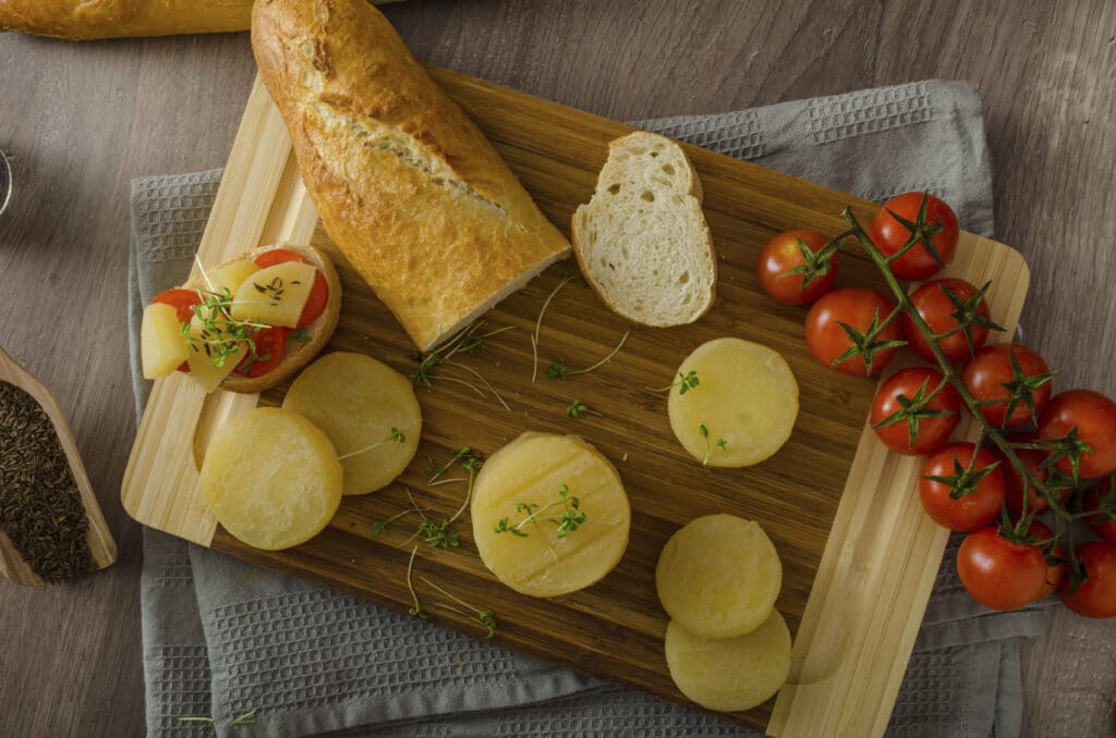 Drevená doštička na ktorej sú položené kolieska syra s paradajkami a begetkou.