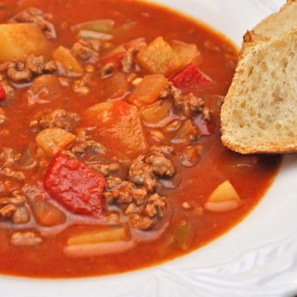 Červená polievka s kúskami zemiakov, pomletého mäsa a zeleniny s plátkom chleba na tanieri
