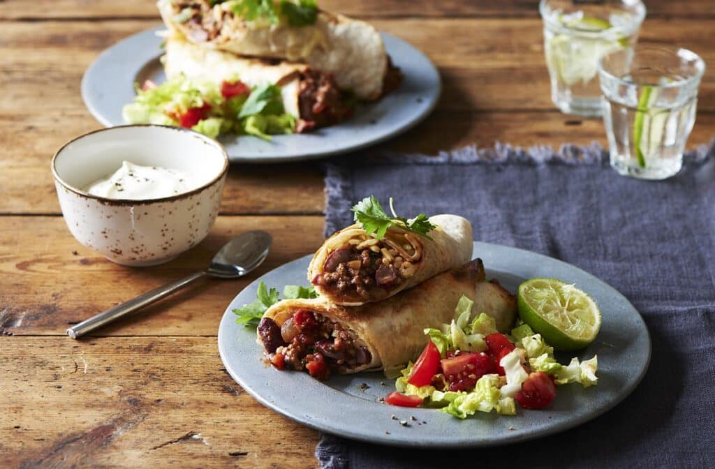 Dva taniere s rozkrojeným hovädzím burritom a zeleninovou oblohou, miska s kyslou smotanou