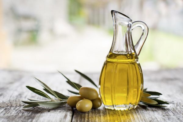 Olivový olej v sklenenej fľaši a vedľa položenej zelenej olivy.