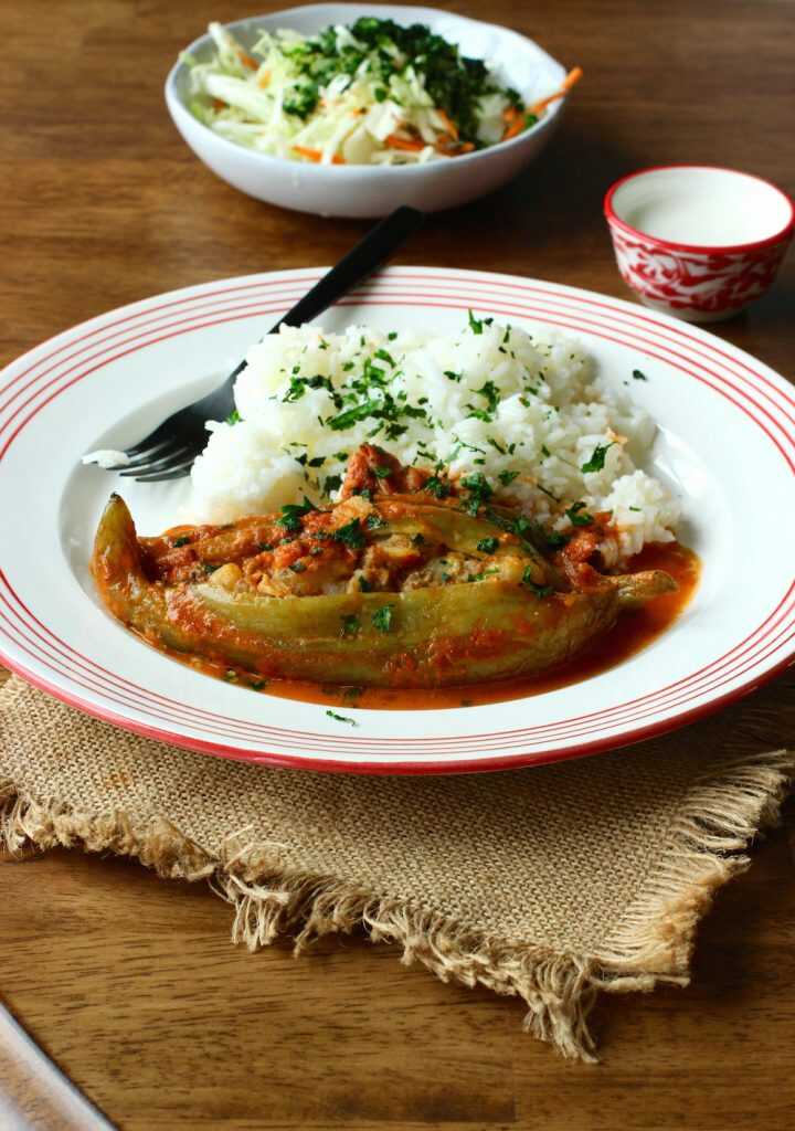 Plnená paprikouhorka s omáčkou a ryžou na tanieri s vidličkou a za tanierom je položený tanier so zeleninou.