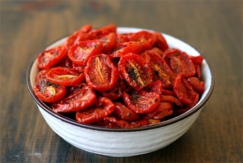 Rozpolené paradajky, usušené v rúre, ochutené bylinkami a podávané v bielej miske.