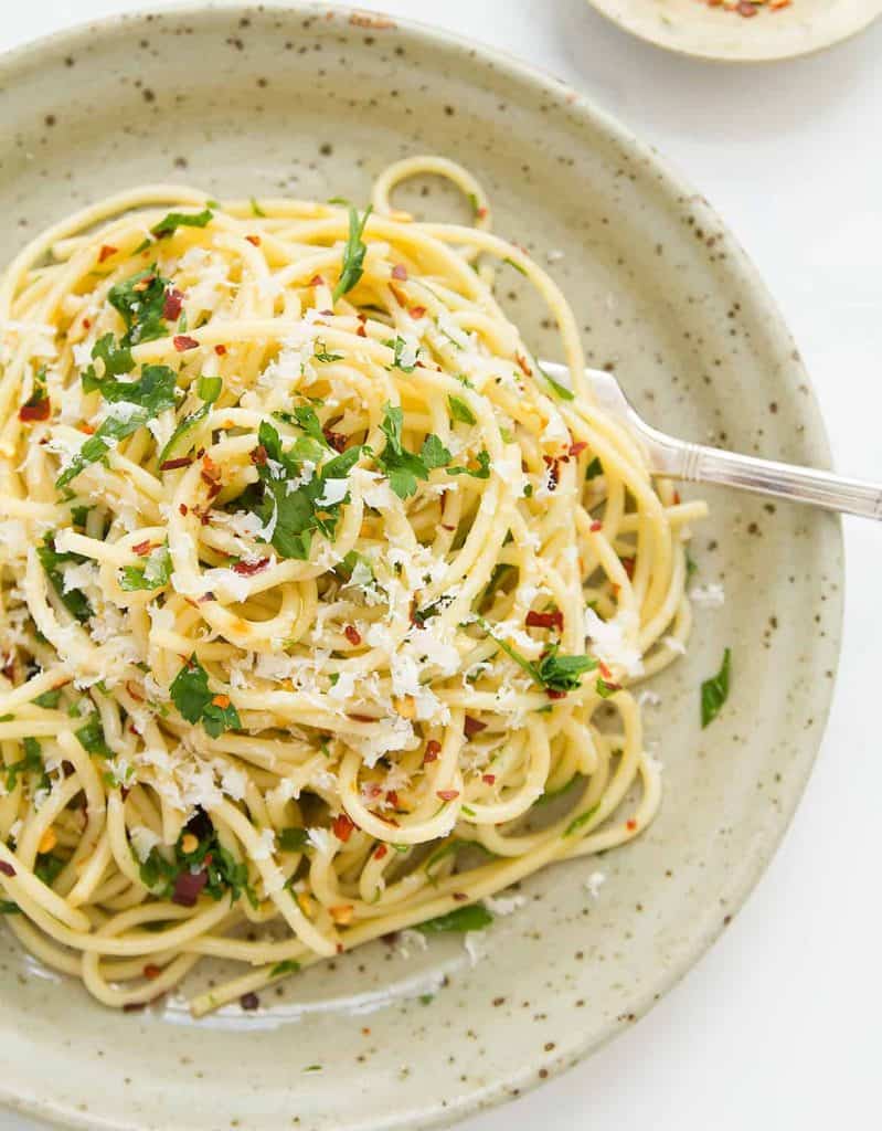 Špagety posypané syrom a petržlenovou vňaťou servírované v hlbokom tanieri s vidličkou.