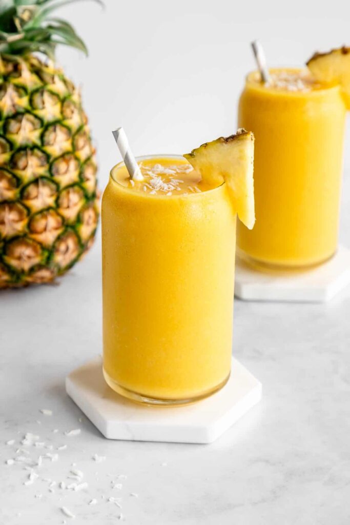 Smoothie z ananásu a kokosového mlieka v pohároch s slamkami ozdobené kúskom ananásu.