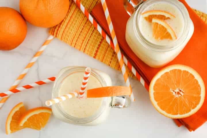 Ovotené smoothie v pohároch s slamkami ozdobené pomarančmi a vedľa sú položené čerstvé pomaranče.