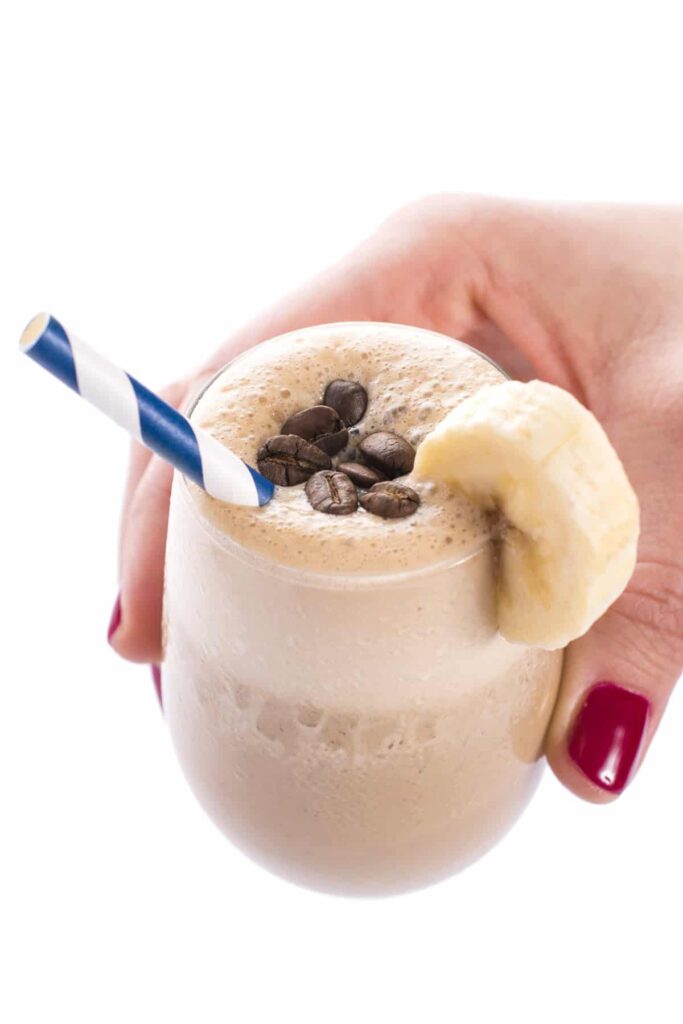 Smoothie z banánu a kávy v pohári so slamkou, ktorú drží ruka.