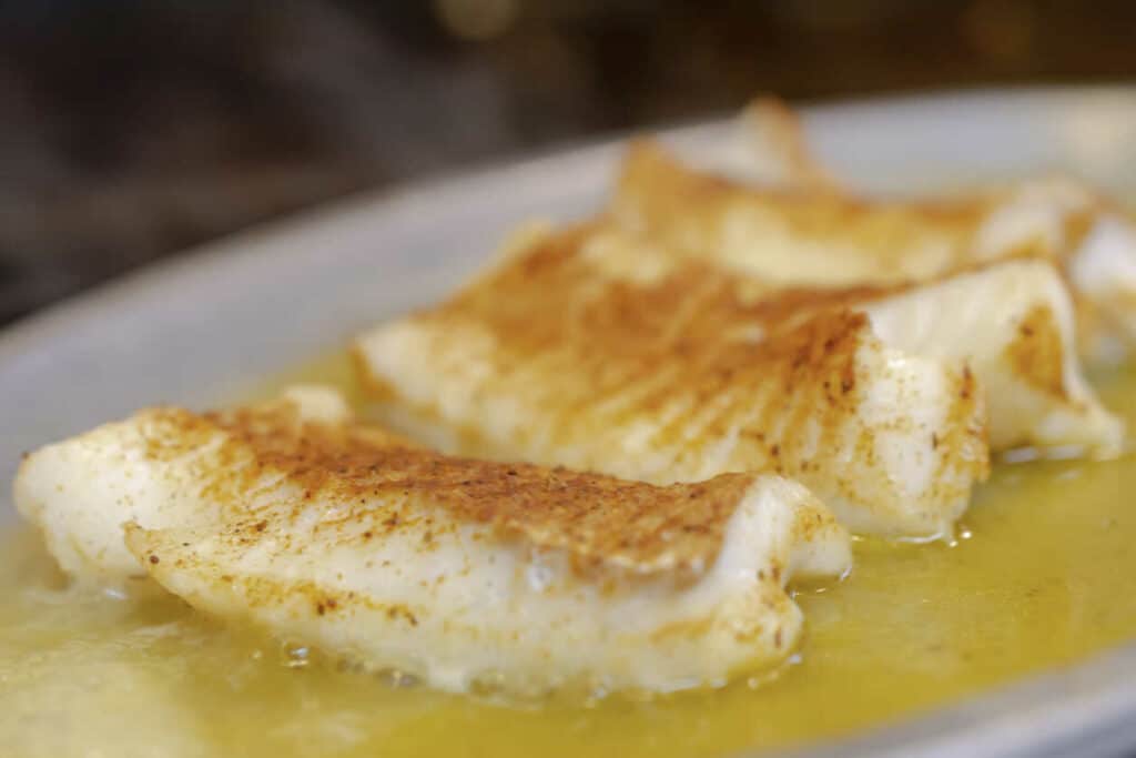Pečená biela ryba na tanieri, preliata omáčkou.