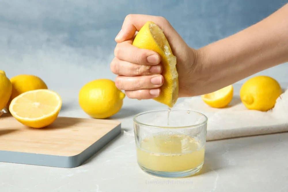 Ruka vytláčajúca citrón do pohára a vedľa položená dosky, na ktorých sú čerstvé citróny.