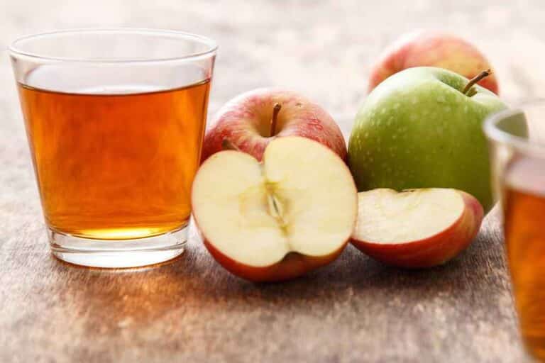 Džús z jabĺk naliaty v pohári, ktorý je položený vedľa čerstvých jabĺk.