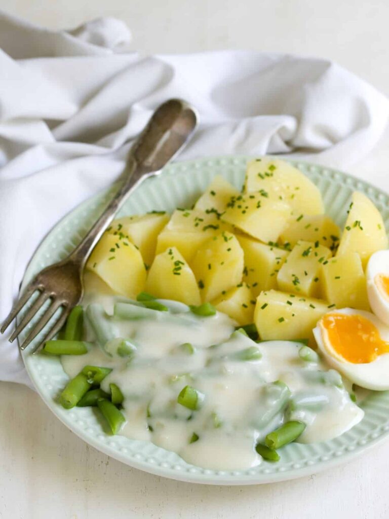 Fazuľky v smotanovej omáčke so zemiakmi a vajcom servírované na tanieri s vidličkou.