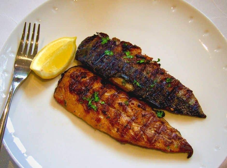 Grilovaná makrela servírovaná na tanieri s klinom citróna a vidličkou.