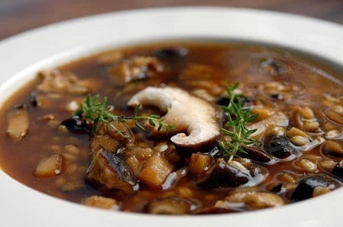 Tmavo hnedá hubová polievka s fazuľkami, zdobená čerstvými vetvičkami rozmarínu.