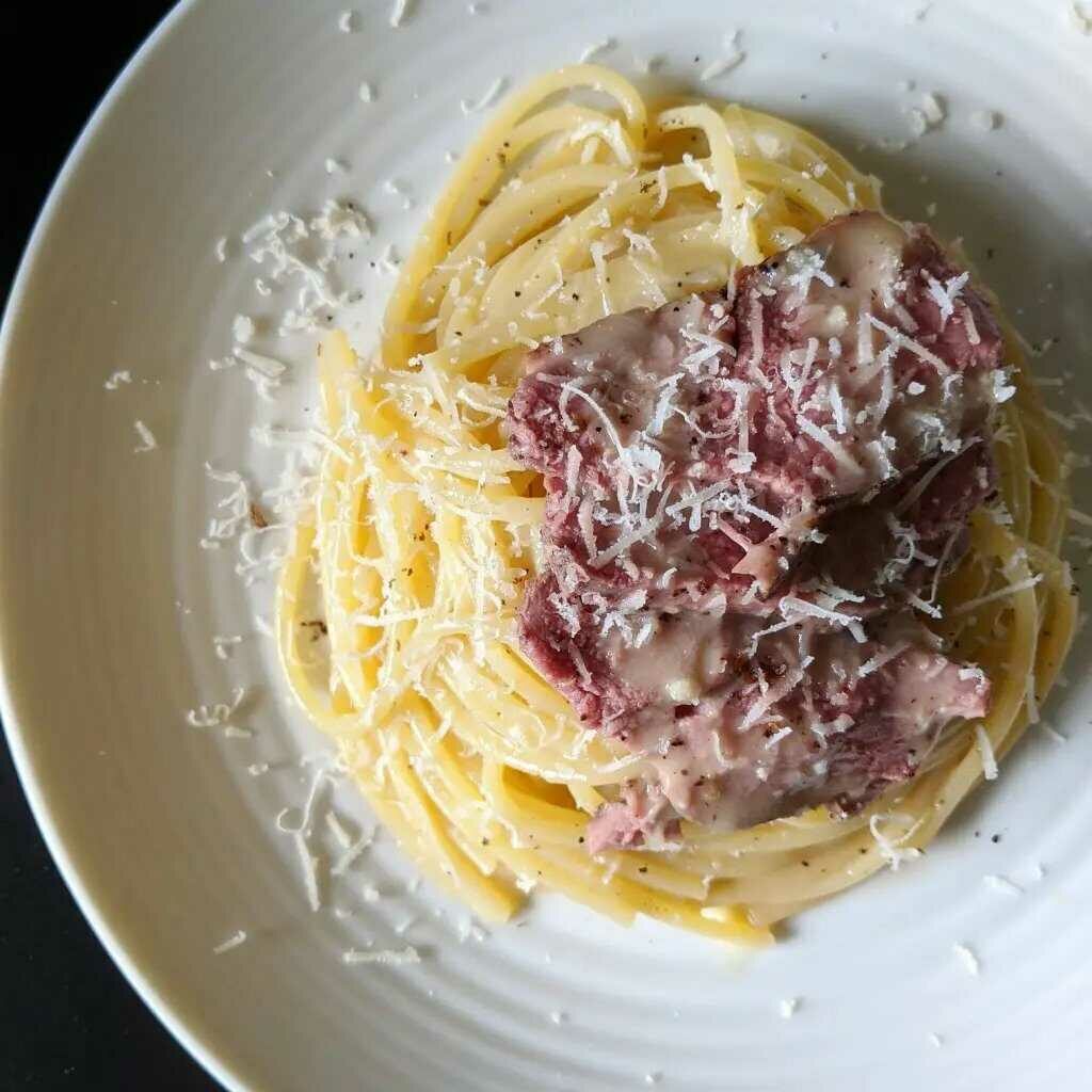 Špagety s kačacím mäsom na tanieri, posypané syrom.