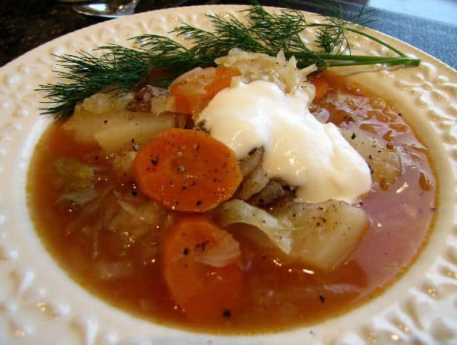 Kapustová polievka so zeleninou, hovädzím mäsom a kyslou smotanou na hlbokom tanieri s kôprom.