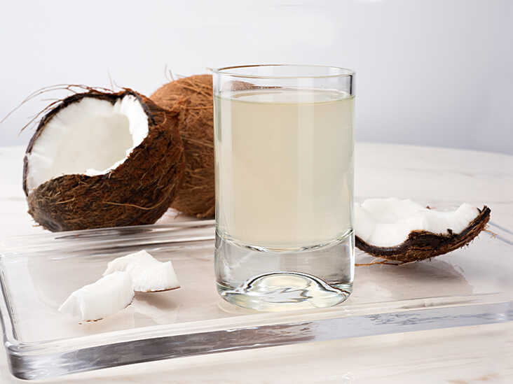 Pohár vody z kokosu a vedľa položenej čerstvej zrelej kokosy.