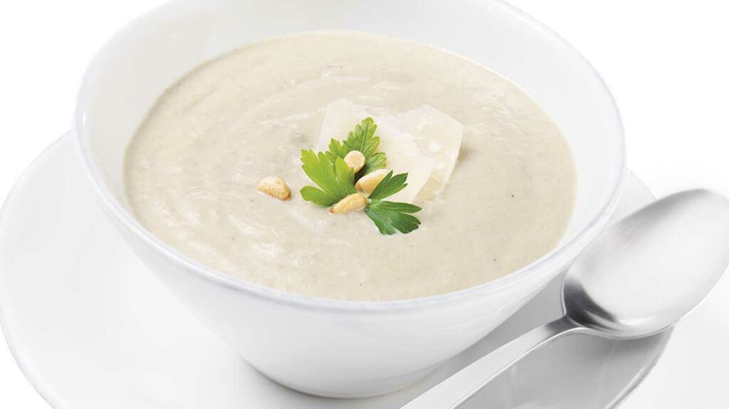 Rozmixovaná krémová polievka z húb v bielej miske so syrom, orieškami a bylinkami.
