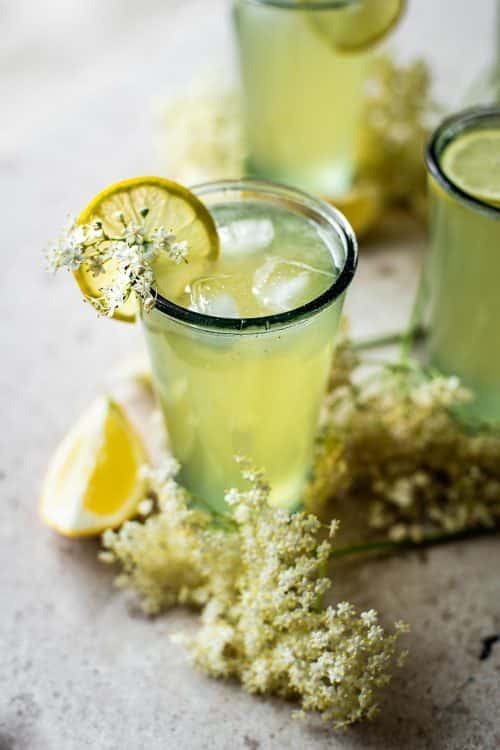 Limonáda z bazových kvetov v pohároch, ozdobená plátkom citróna a čerstvými kvetmi.