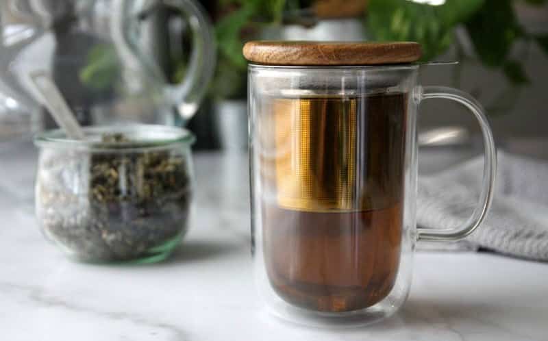 Maliníkový čaj v sklenenom hrnčeku s vedľa položenou sušenou zmesou.