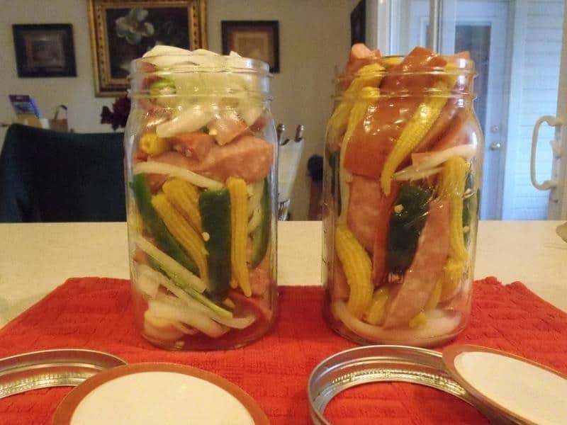 Klobásy naložené v pohároch so zeleninou.