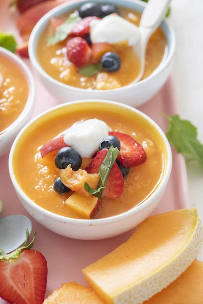 Melónová polievka v mištičkách, ozdobená čerstvým ovocím a jogurtom.
