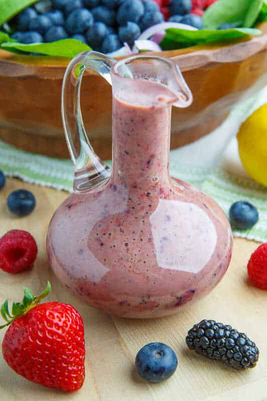 Dresing z gréckeho jogurtu, lesného ovocia, maku a bieleho balzamiku v sklenenej fľaši s vedľa položeným ovocím.