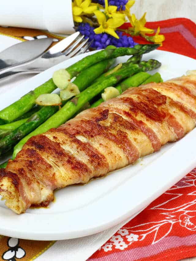 Ryba zabalená v slanine, podávaná so špargľou a strúčikmi cesnaku.