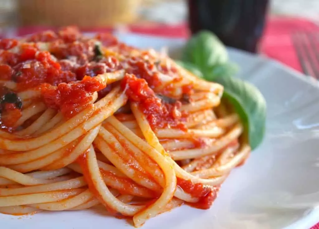 Špagety s paradajkovou omáčkou servírované na tanieri s lístkami bazalky.