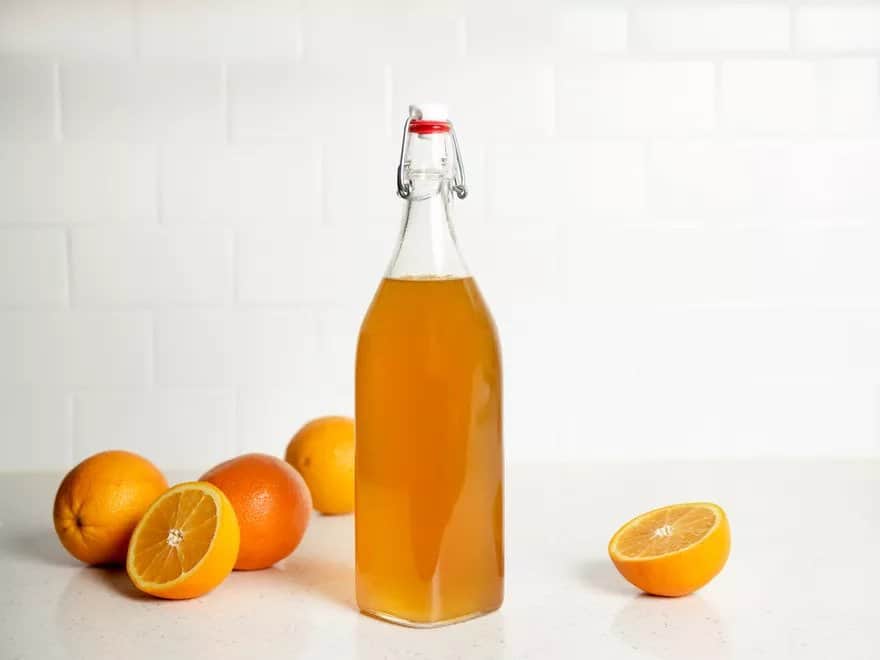 Likér z pomarančov v sklenenej fľaši a vedľa sú položené čerstvé pomaranče.