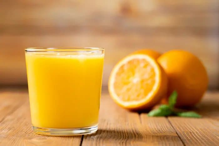 Šťava z pomarančov v pohári av pozadí sú čerstvé pomaranče.