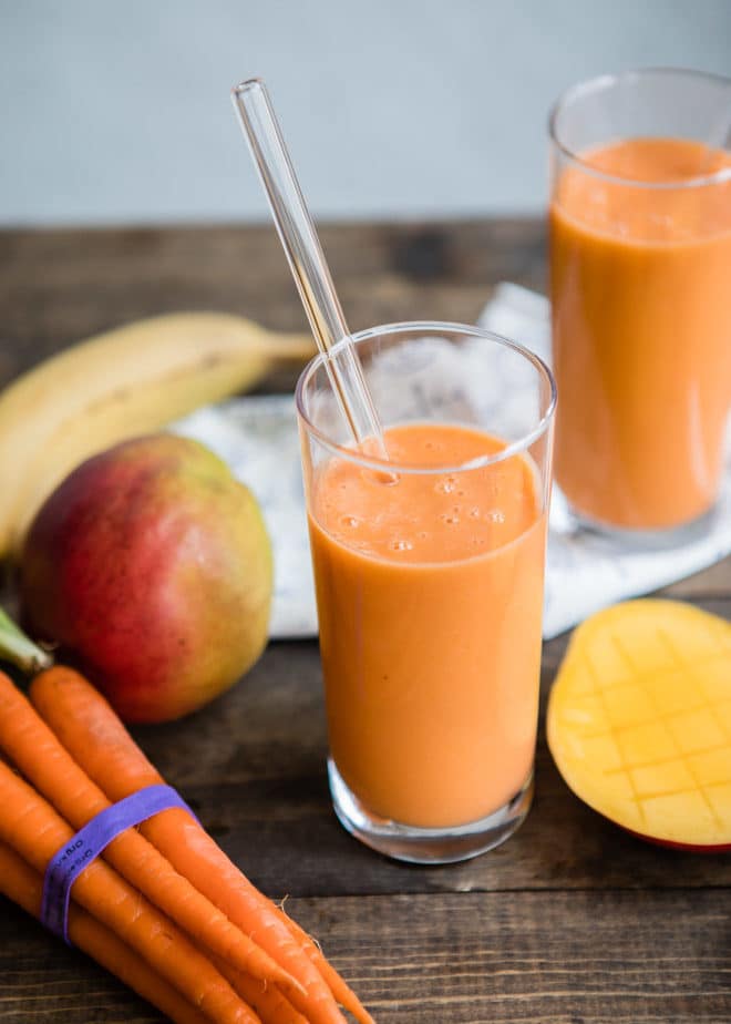 Ovocno-zeleninové smoothie v pohári so slamkou s vedľa položenou mrkvou, mangom a banánom.