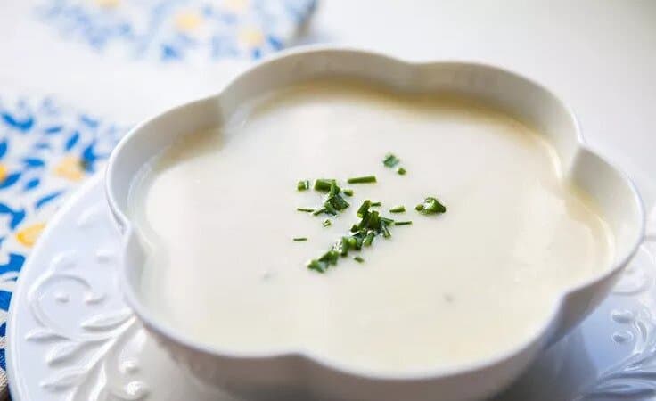 Francúzska polievka Vychyssoise servírovaná v mištičke a ozdobená čerstvou bylinkou.