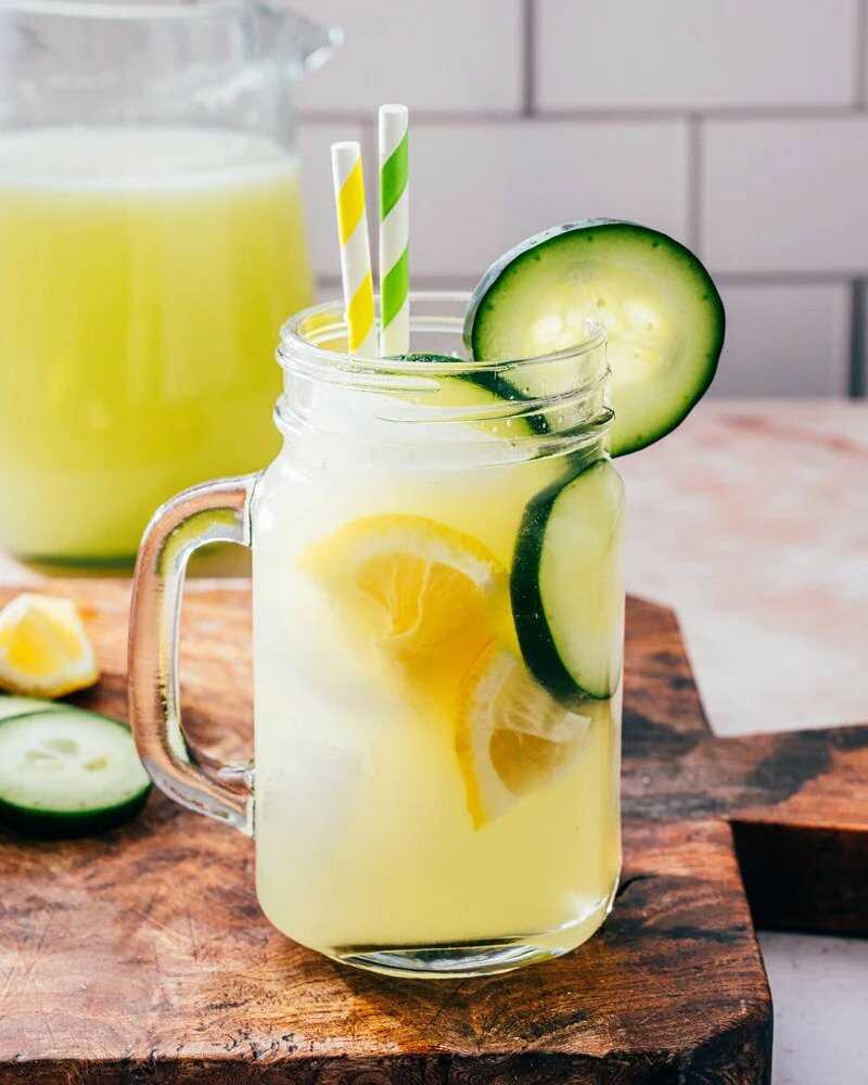 Limonáda z uhoriek v pohári s slamky, plátky uhorky a klinky citróna.