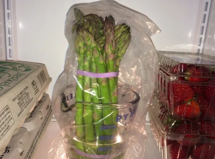 Zelená špargľa uskladnená v chladničke v pohári a zakrytá igelitovým vreckom.