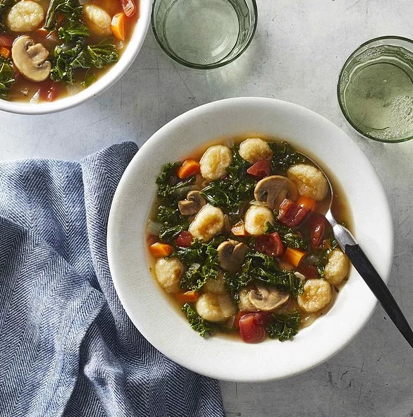 zeleninová polievka s gnocchi s hubami, paradajkami a mrkvou v bielej miske s lyžičkou