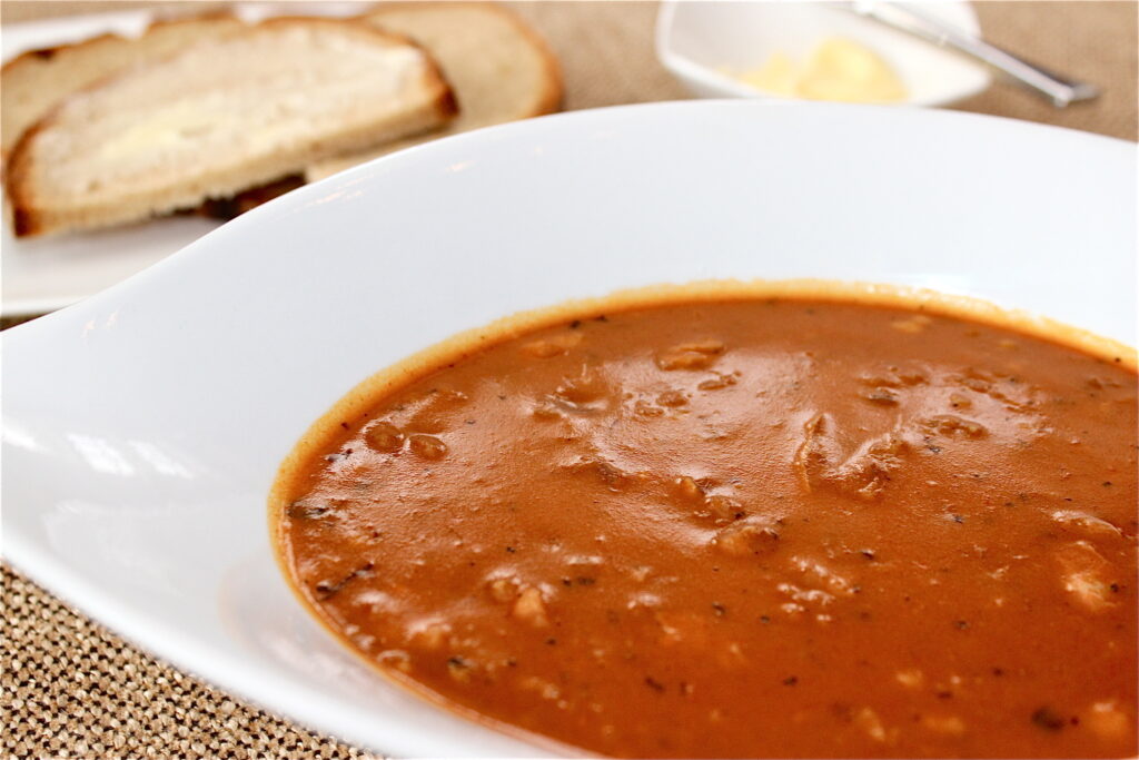 Tradičná polievka s držkami, paprikou, majoránom a chlebom v bielom tanieri.