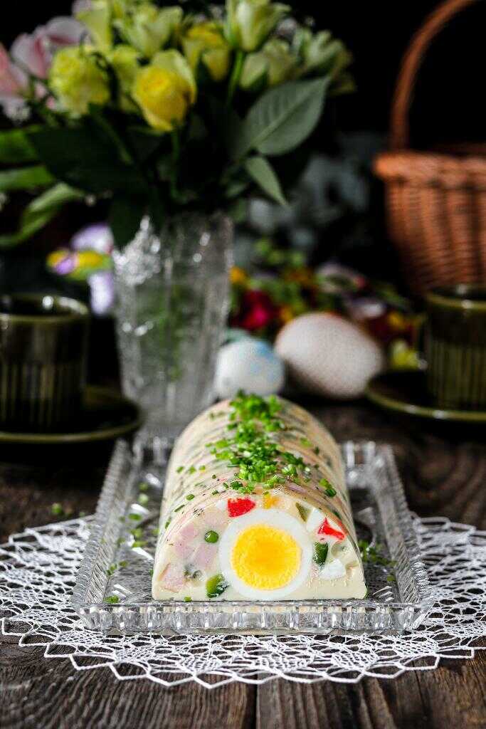 Tlačenka plnená zeleninou, salámou a celými vajcami servírovaná na sklenenej tácke a ozdobená čerstvými bylinkami.