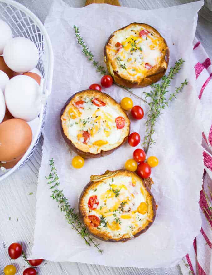 Vajíčka pečené v rúre v chlebových hrčkach so syrom, bylinkami a paradajkami, servírované na obrúsku s čerstvými cherry paradajkami a vetvičkami tymiánu.