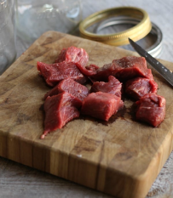 Kocky surového mäsa na drevenom lopári s nožom.