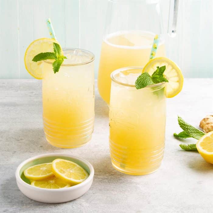 Limonáda zo zázvoru v pohároch so slamkou, ozdobená čerstvou mätou a plátkom citróna.
