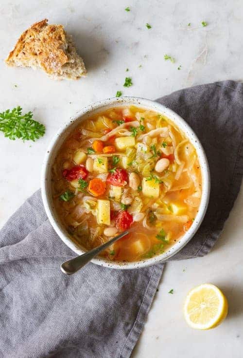 Zeleninová polievka s bielymi fazuľami v hlbokom tanieri s lyžicou.