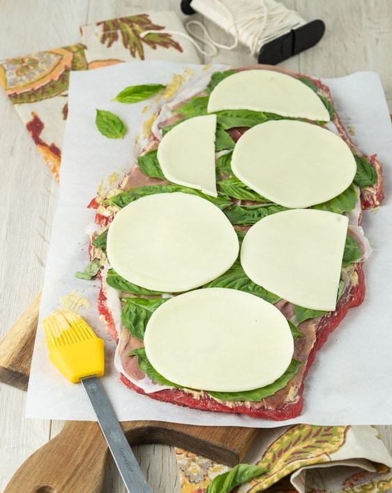 Rozprestretý plátok mäsa naplnený zelenou rukolou a syrom.