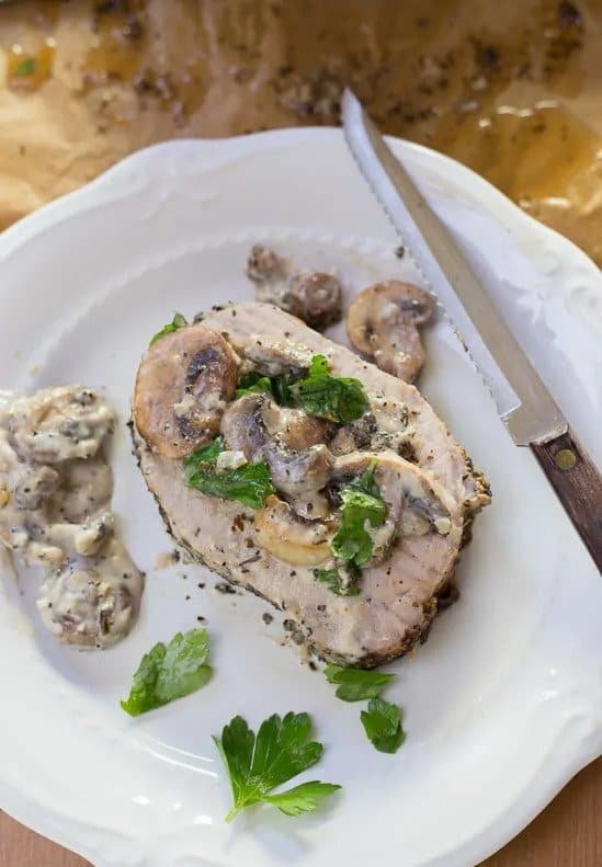 Bravčové mäso pečené na cesnaku a bylinkách a preliate bohatou šampiňónovou omáčkou na tanieri s nožom.